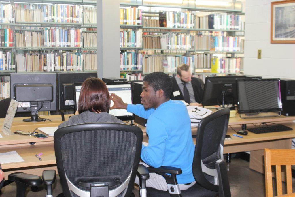 Two 学生 using in a computer in the library computer lab.